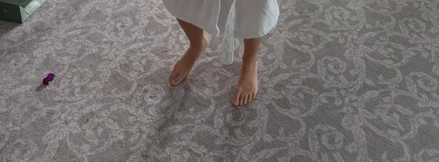 Emily Ratajkowski standing barefoot on a patterned carpet.