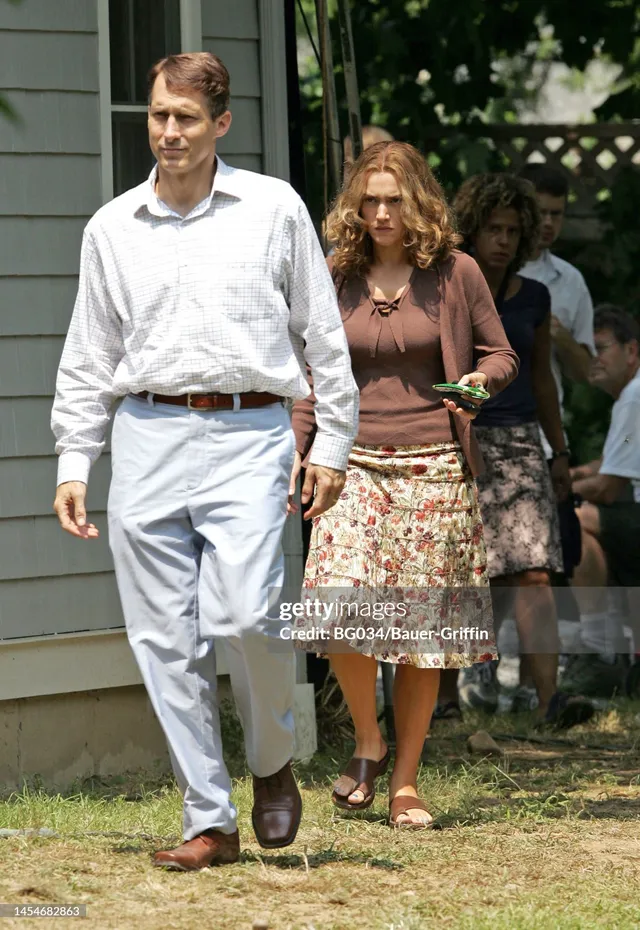 Kate Winslet walking outdoors in a floral skirt beside a companion.