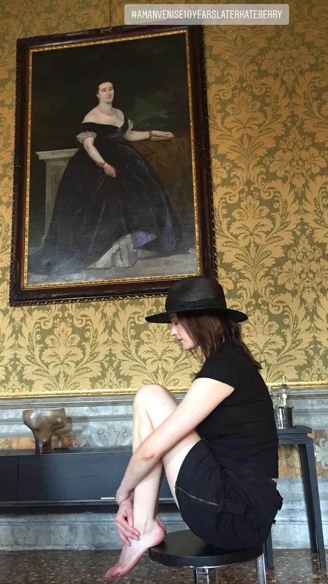 Eva Green seated on a stone ledge in a dark outfit and hat.