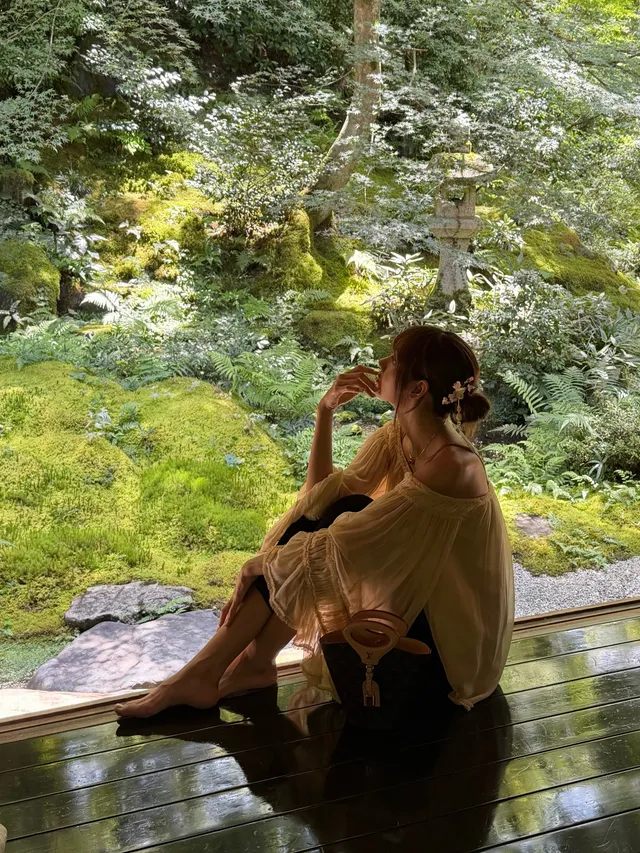 Lisa (Lalisa Manobal) sitting barefoot on a wooden terrace beside a garden.