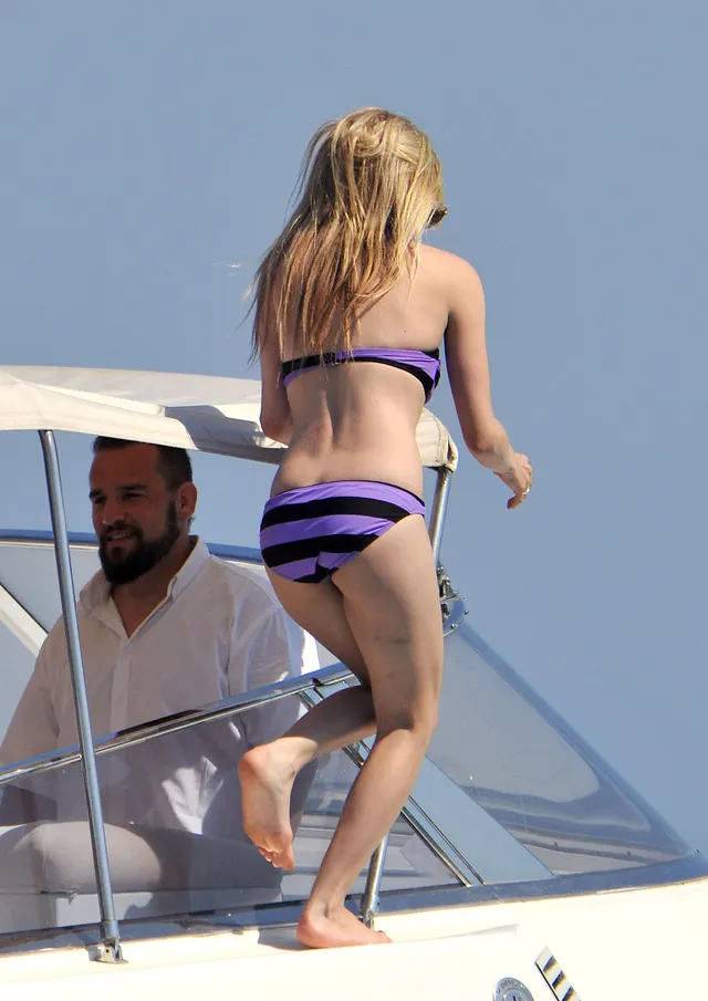 Avril Lavigne walking barefoot on a boat in a striped swimsuit.
