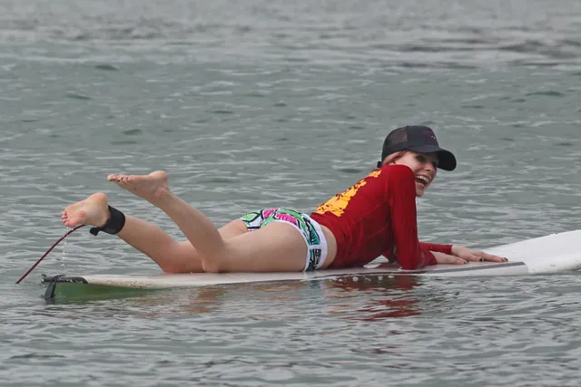 Avril Lavigne lying barefoot on a paddleboard on the water.