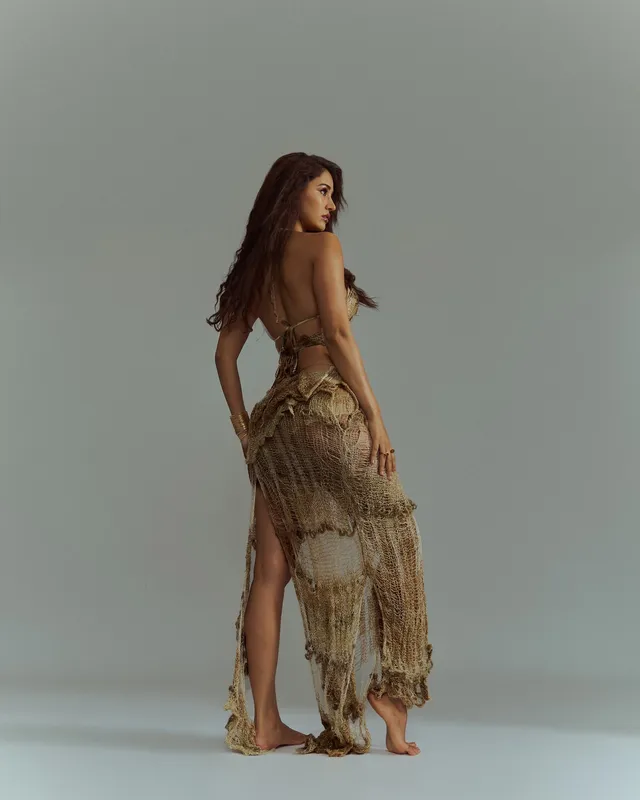 Disha Patani standing barefoot in a fringed gold outfit during a studio shoot.