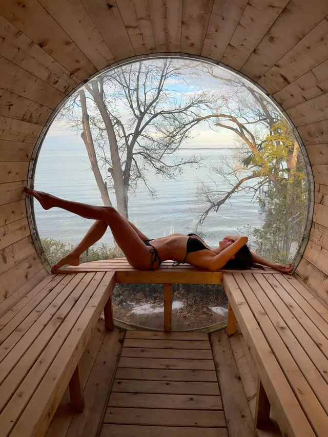 Nina Dobrev reclining barefoot on a bench beside a circular window.