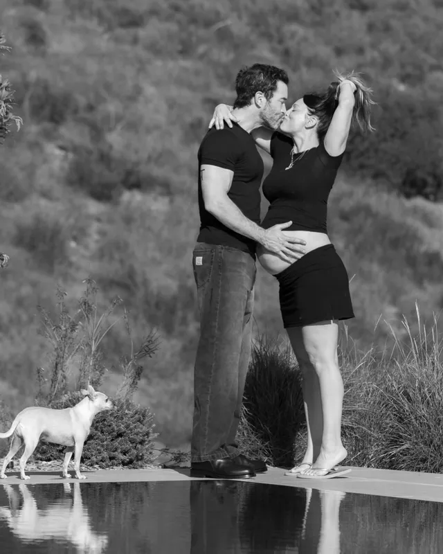 Kaley Cuoco standing barefoot beside another person in a monochrome outdoor portrait.