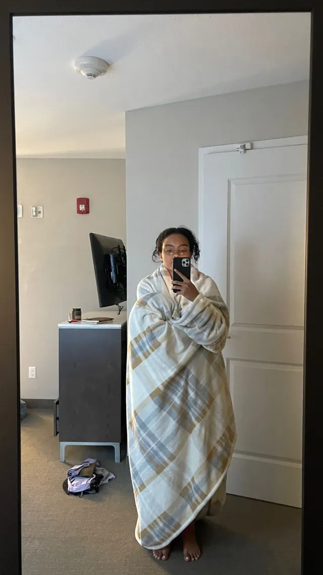 Whitney Peak taking a mirror selfie wrapped in a blanket while wearing dark slides.