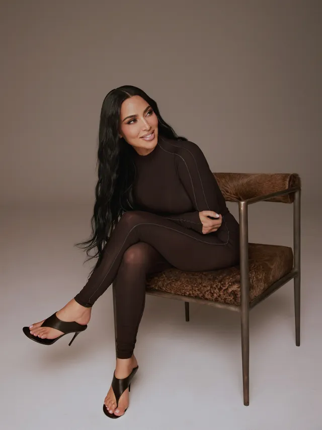 Kim Kardashian: seated on a chair in a dark outfit and black heels.