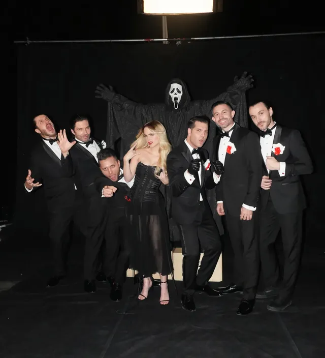 Mckenna Grace posing beside a group in a dark dress and heels.