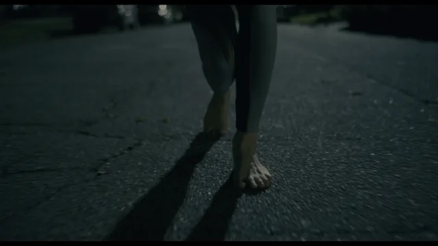 Rebecca Ferguson standing barefoot on a dark street in a film close-up.