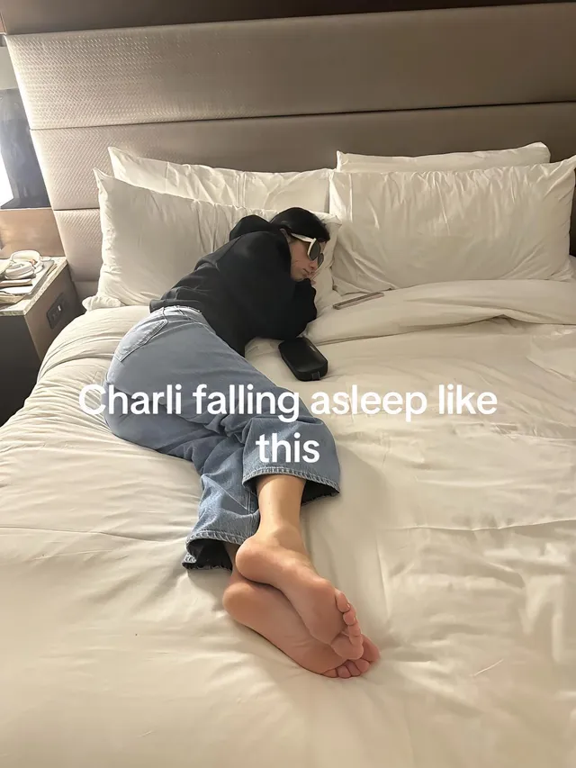 Charli D’Amelio lying on a bed in jeans with bare soles visible.
