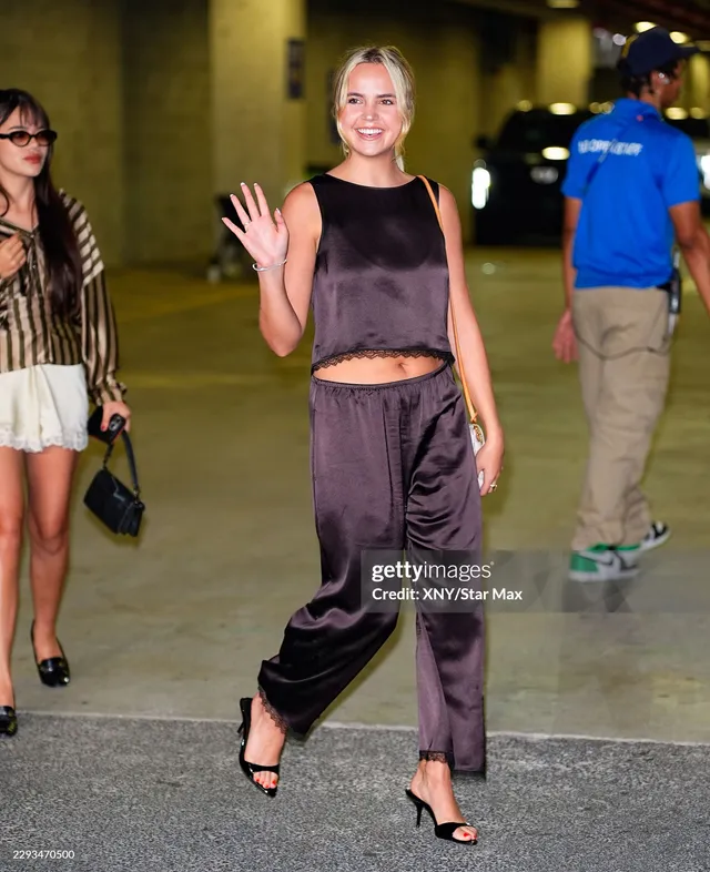 Bailee Madison walking in a dark satin outfit and heels.