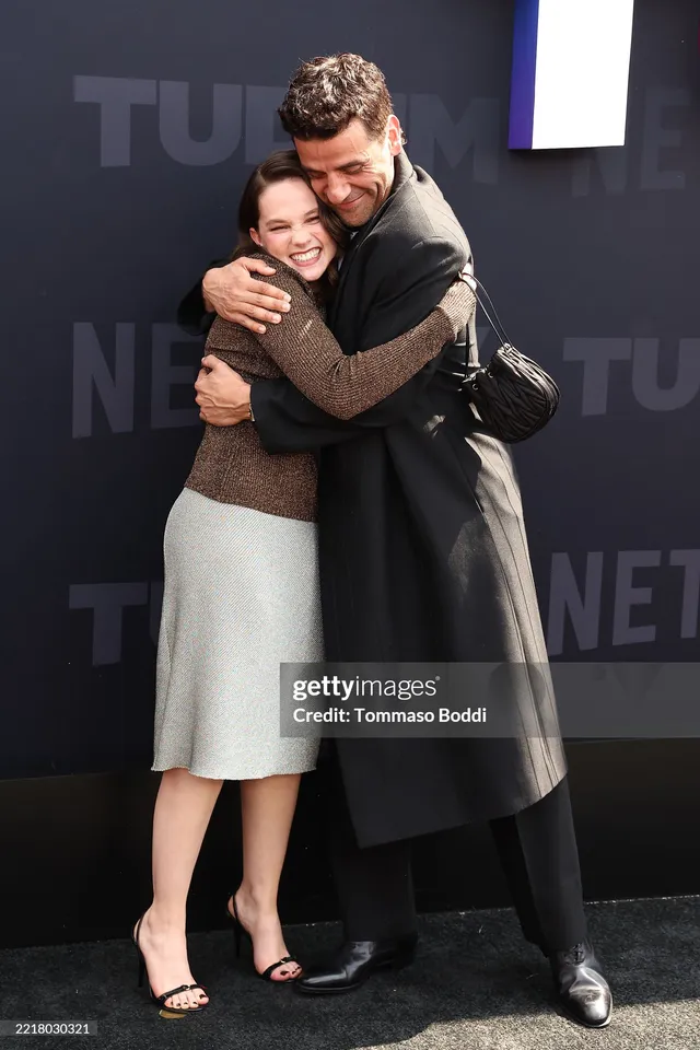 Cailee Spaeny hugging a man at an event in a grey skirt and heels.