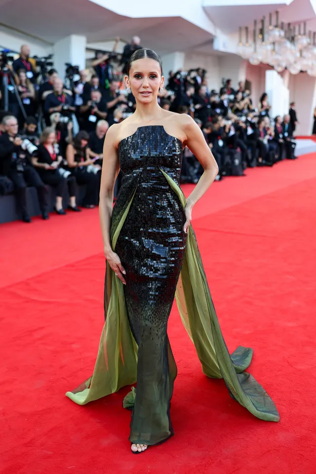 Nina Dobrev posing in a dark gown on a red carpet.