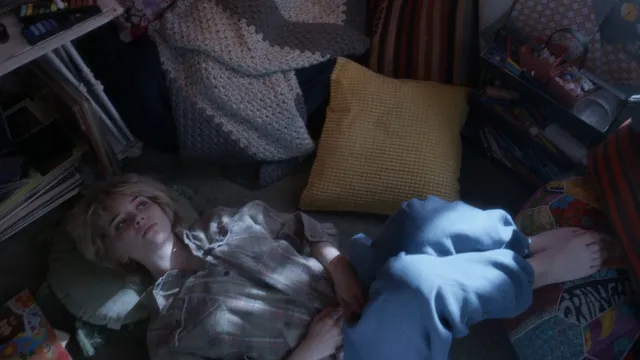 Sophie Thatcher lying among books on a floor in a film scene.