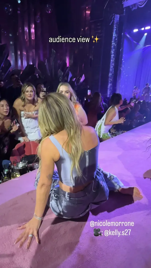 Hilary Duff sitting onstage in a silver dress and heels.
