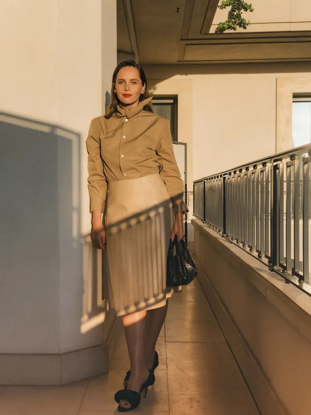 Felicity Jones posing on a balcony in a beige outfit.