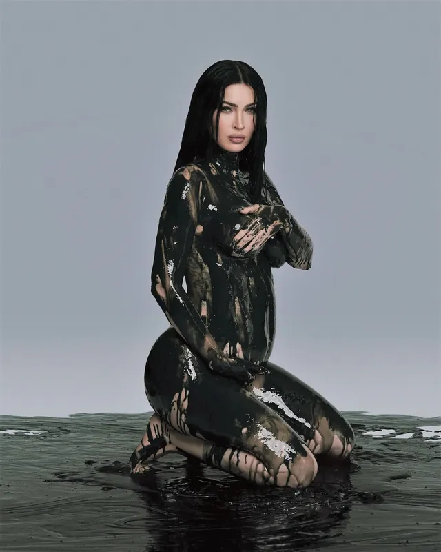 Megan Fox kneeling in shallow water in a patterned outfit.
