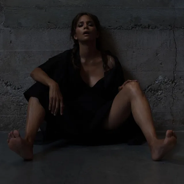 Halle Berry sitting barefoot in a dark outfit.