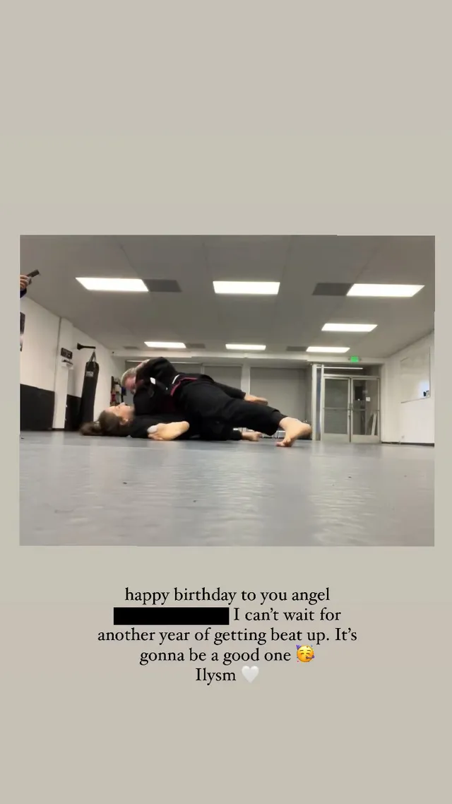 Chloë Grace Moretz reclining barefoot on a gym floor beside another person.