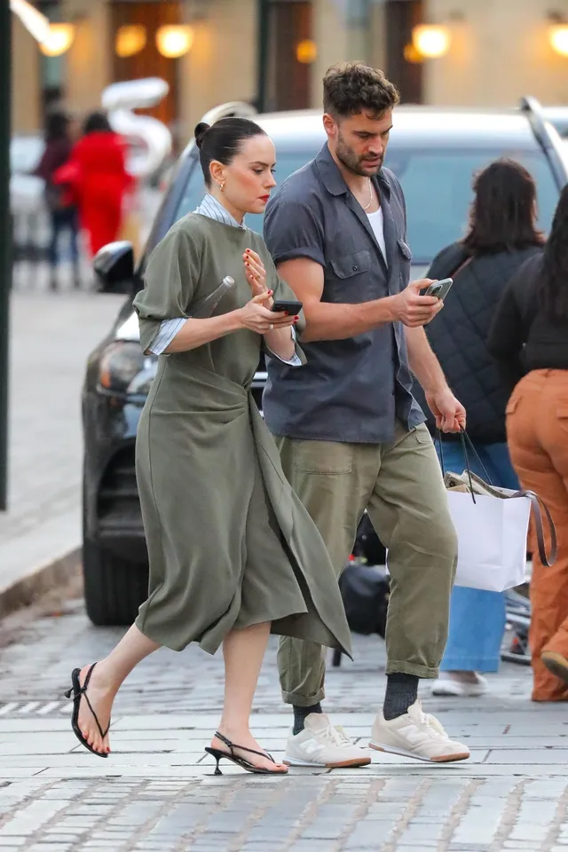 Daisy Ridley crossing a street in a green dress and sandals.