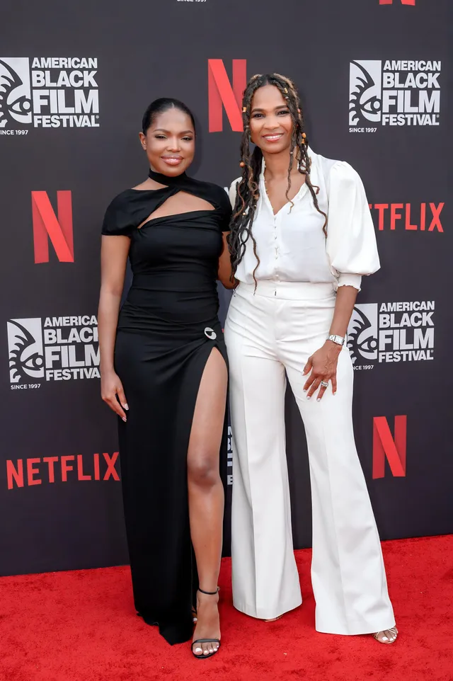 Ryan Destiny posing beside a guest in a black dress and heels at an event.