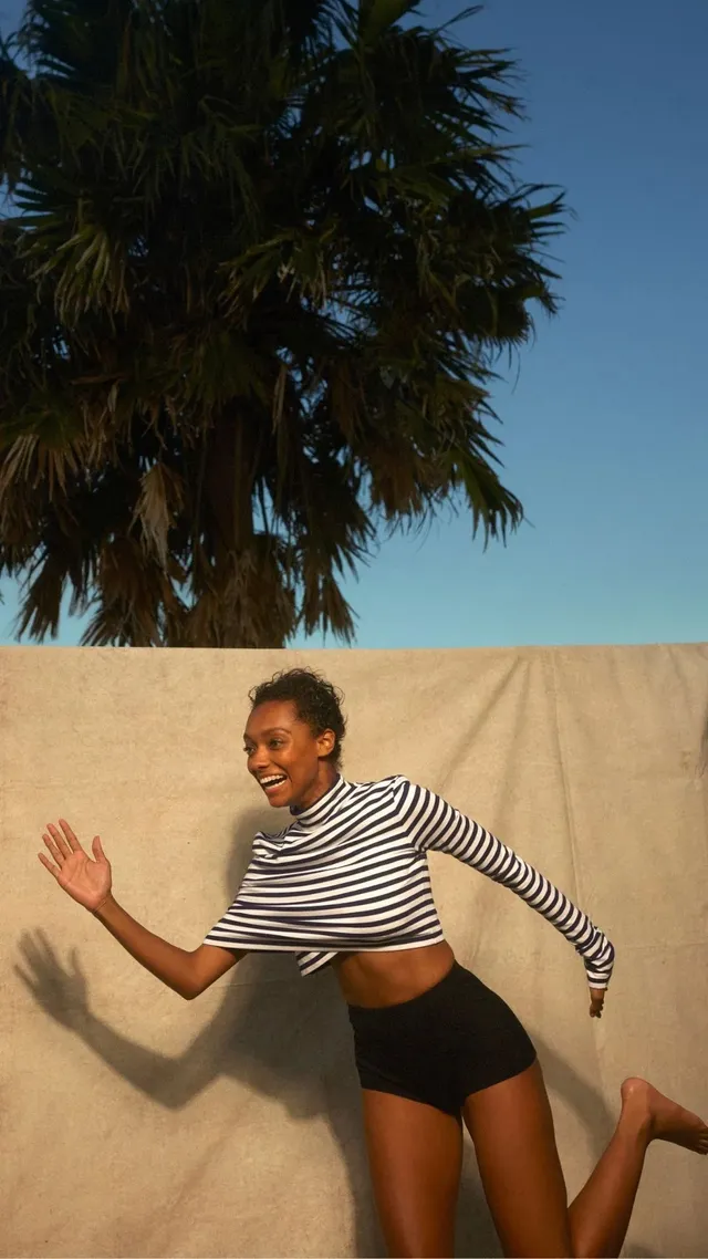 Sophie Wilde jumping barefoot beside a wall in a striped top.