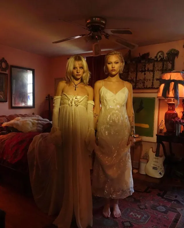 Grace VanderWaal posing beside another woman in pale dresses indoors.