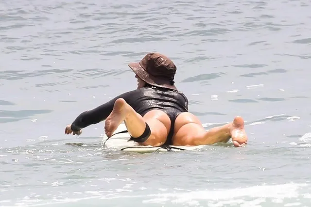 Leighton Meester paddling through the sea on a surfboard.