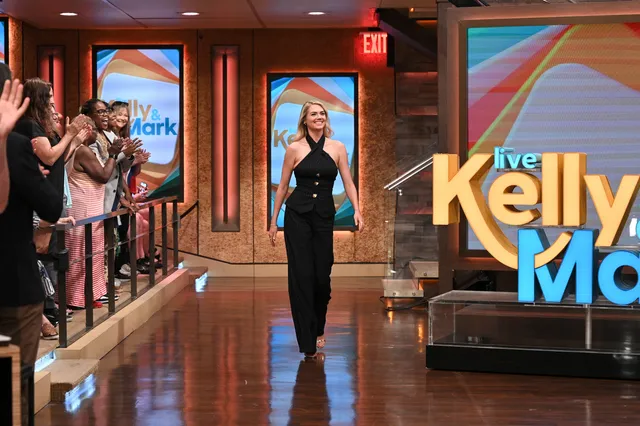 Kate Upton walking onto a television set wearing a black outfit.
