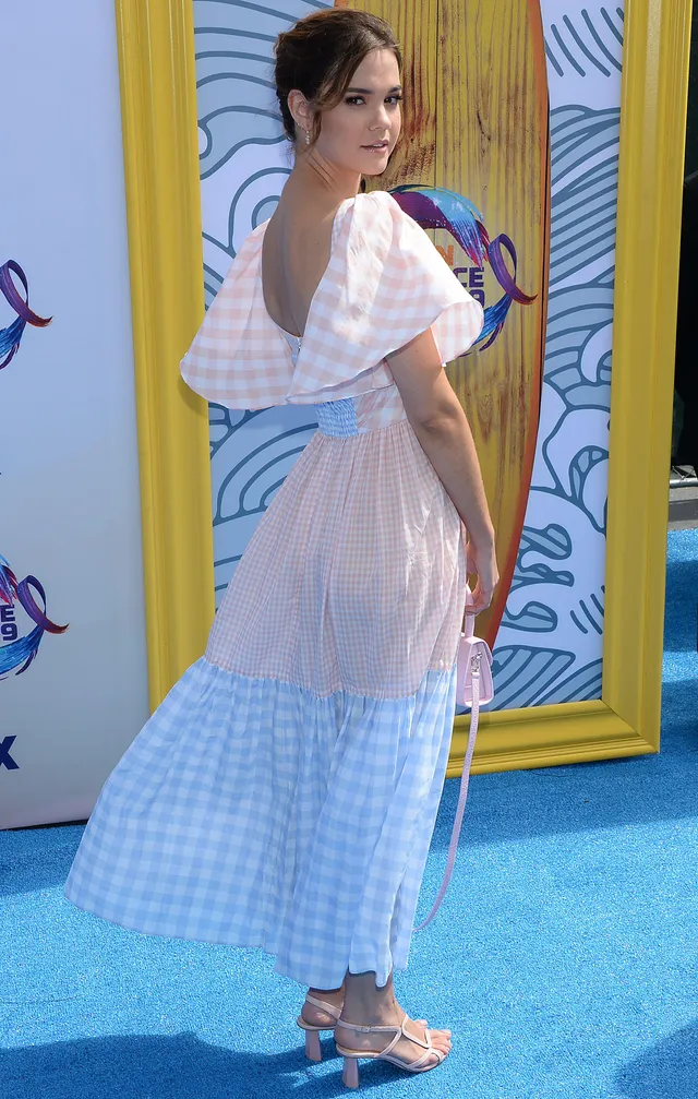 Maia Mitchell wearing a pastel dress and pale heels on a blue carpet.
