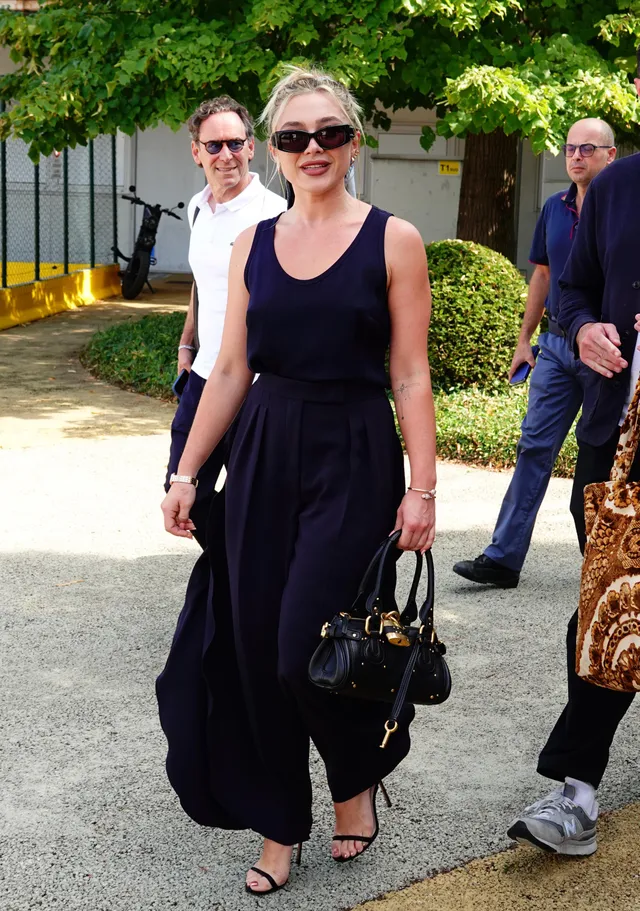 Florence Pugh walking outside in a dark outfit and strappy heels.
