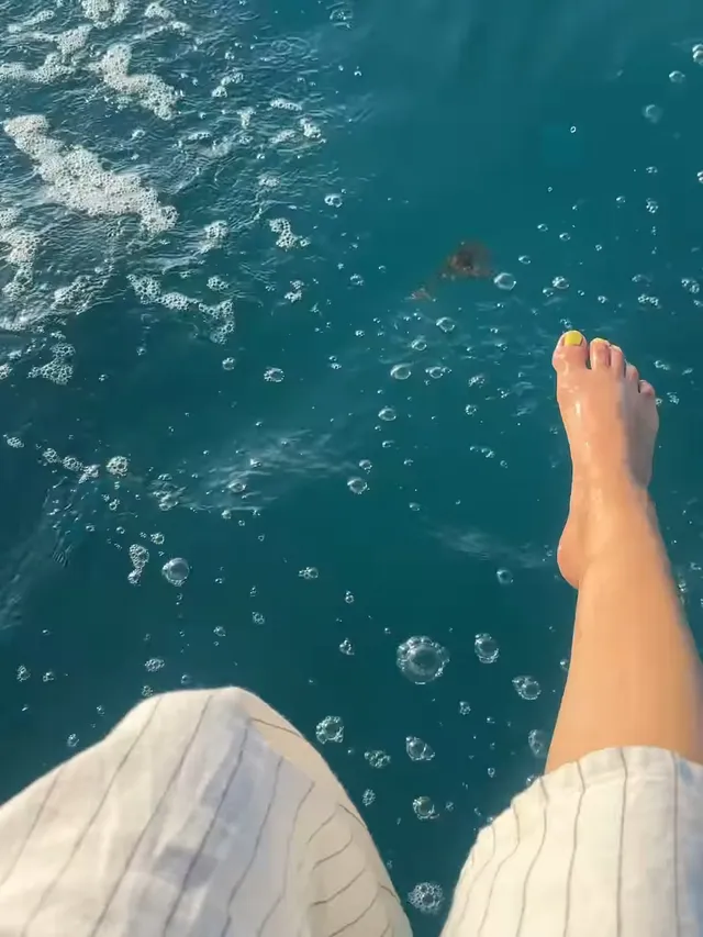 Victoria Justice resting a bare foot above blue seawater from a boat.