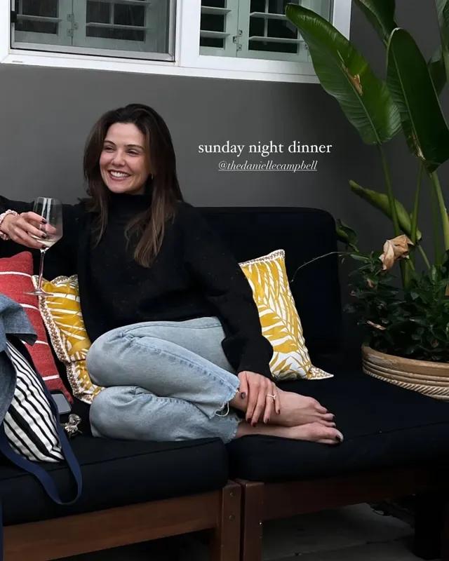 Danielle Campbell sitting cross-legged on an outdoor sofa.