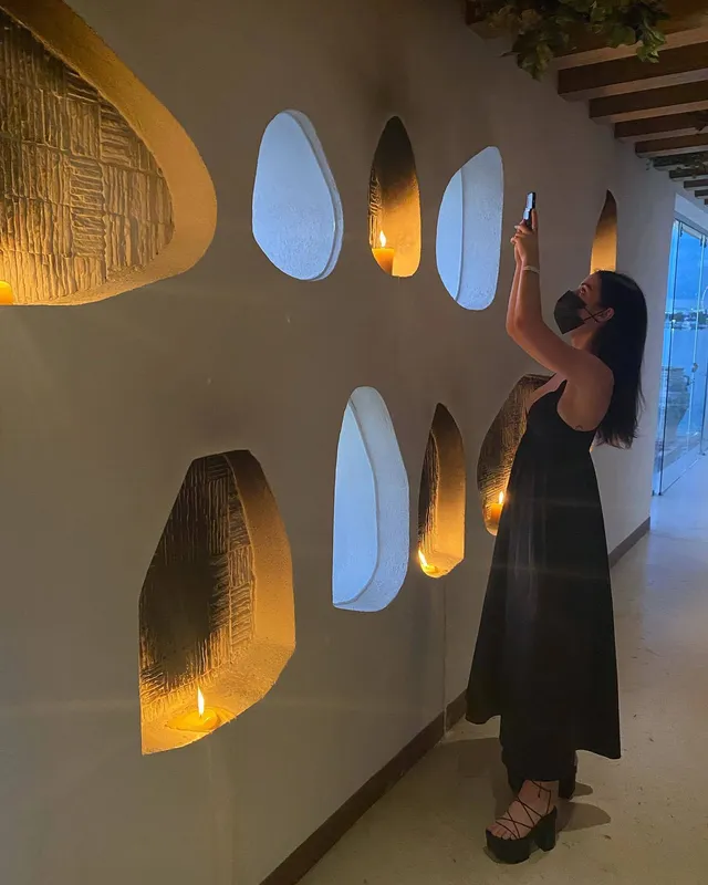 Adelaide Kane standing indoors in a long dark outfit and flat sandals.