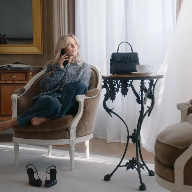 Samara Weaving sitting barefoot in an armchair beside a pair of heels.