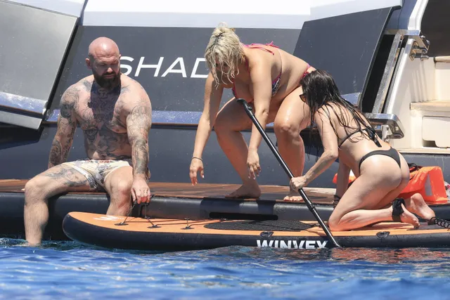 Bebe Rexha climbing barefoot between a boat and paddleboard.