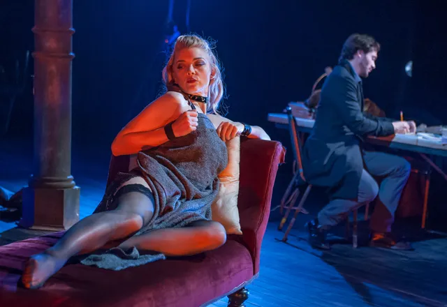 Natalie Dormer reclining on a chaise beside another performer onstage.