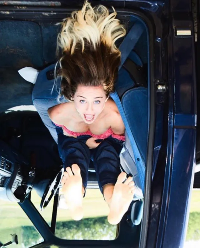 Miley Cyrus raising bare soles during an outdoor photograph.