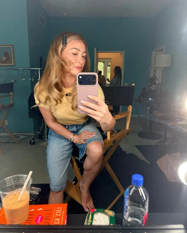 Hilary Duff taking a barefoot mirror photo while seated in a chair.
