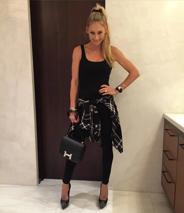 Anna Kournikova standing in pointed heels, black leggings and a black top.