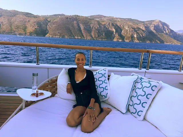 Zoe Saldaña kneeling on a boat sofa beside a sea view.