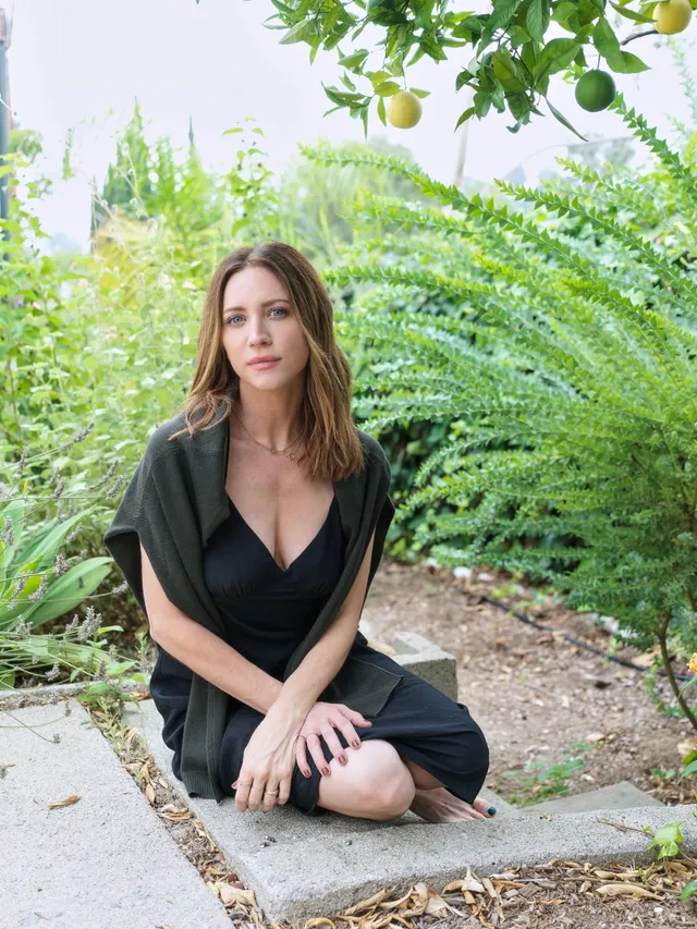 Brittany Snow sitting beside a garden path in a black dress.