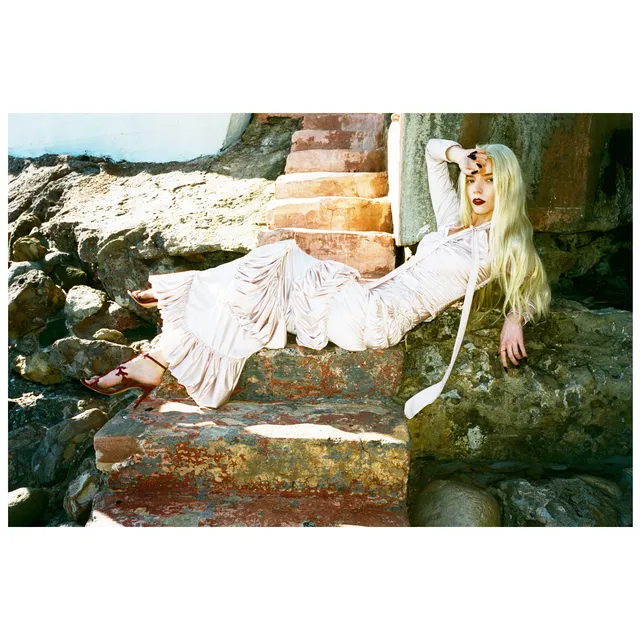 Anya Taylor-Joy reclining barefoot on stone steps in a flowing dress.