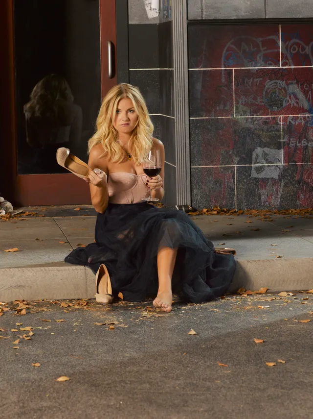Elisha Cuthbert sitting barefoot on steps while holding a glass.