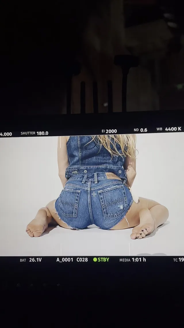 Addison Rae kneeling barefoot in a denim outfit on a photo set.