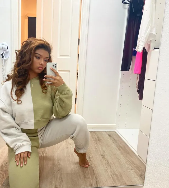 Sierra Capri posing barefoot in a pale tracksuit for a mirror selfie.