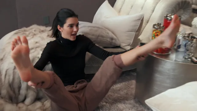 Kendall Jenner sitting on a sofa with bare feet extended.