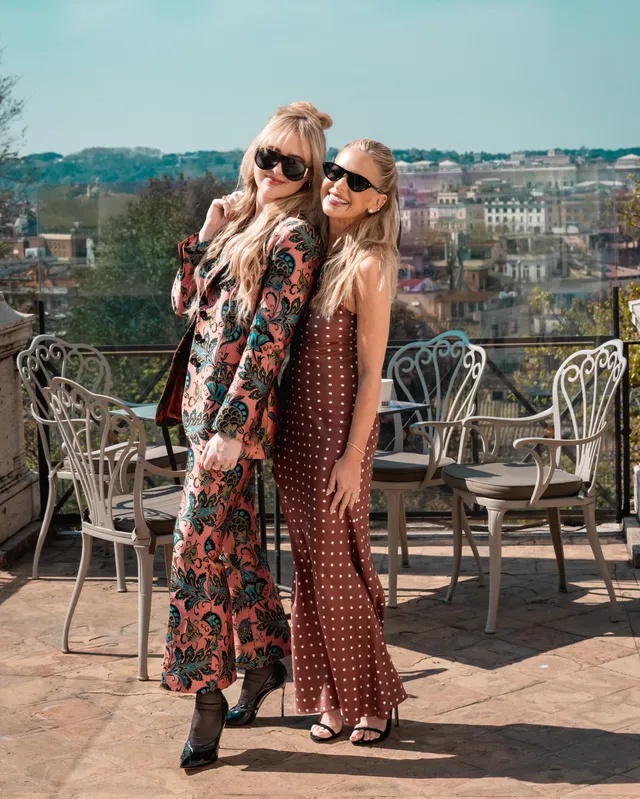 Sarah Michelle Gellar standing beside another person on a terrace in a patterned dress and heels.