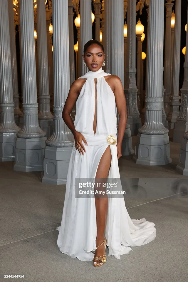 Ryan Destiny posing in a pale halter gown and gold heels at an event.