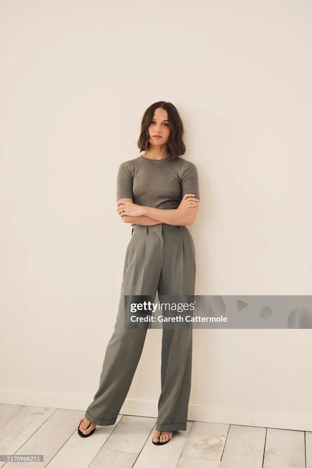 Alicia Vikander posing in a grey trouser suit.